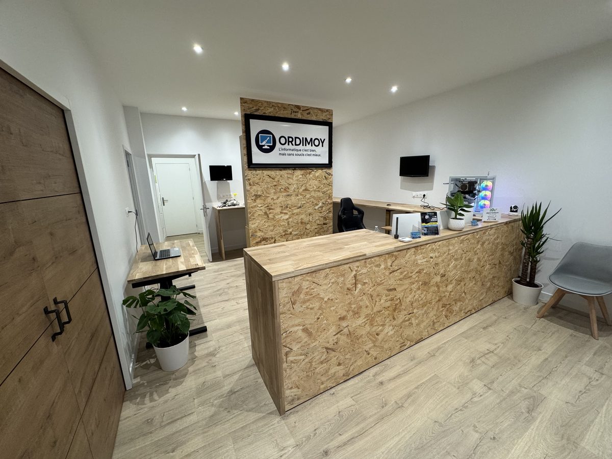 Intérieur de l'atelier Ordimoy : comptoir d'accueil en OSB, espace de réception clair, plantes et chaises